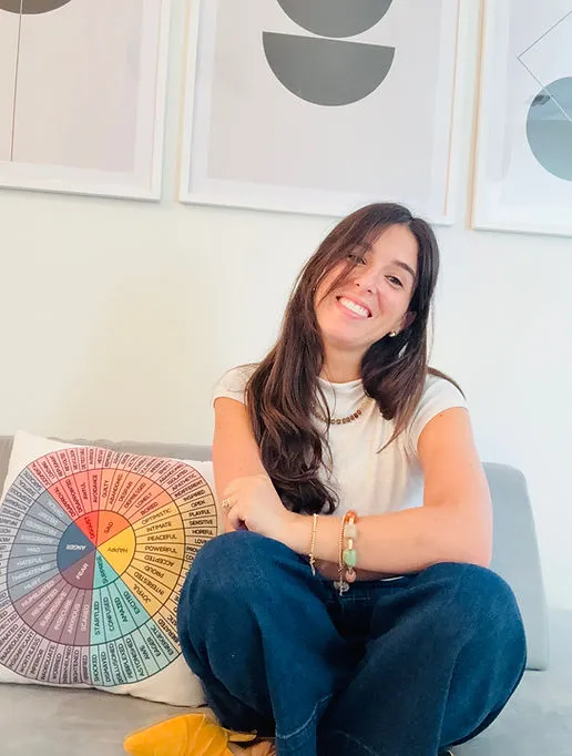 Samantha seated on a couch beside a colorful feelings wheel pillow