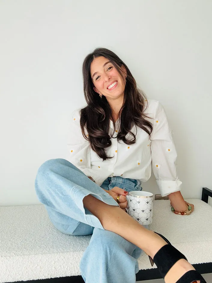 Samantha seated in a white blouse and jeans, holding a mug and smiling